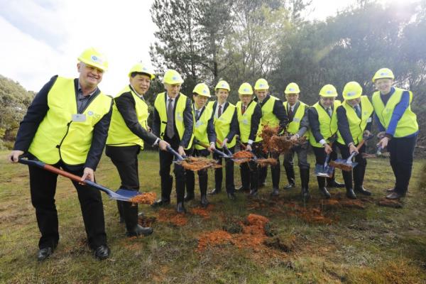 Officials including wearing high visibility gear break first ground with shovels on a grassy field.